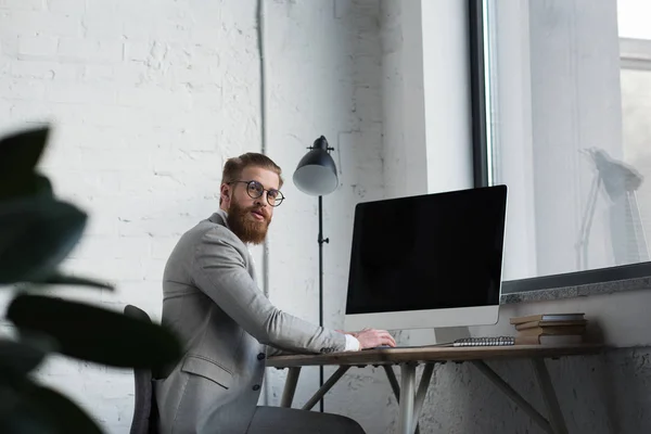 Geschäftsmann sitzt mit Computer am Tisch und blickt in Kamera — Stockfoto