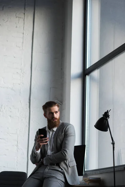 Empresário segurando smartphone e olhando para longe — Fotografia de Stock