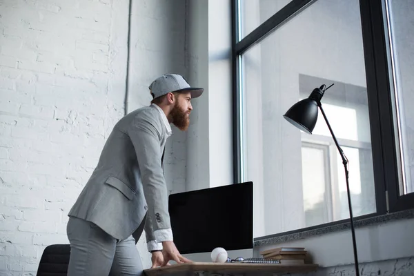 Businessman in baseball cap looking at window in office — Stock Photo