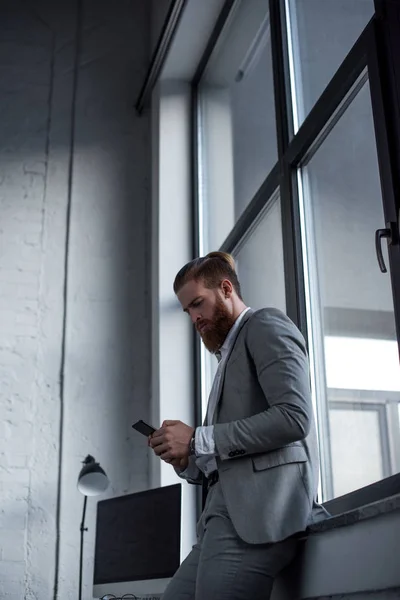 Vue du bas de bel homme d'affaires en utilisant le smartphone dans le bureau — Photo de stock