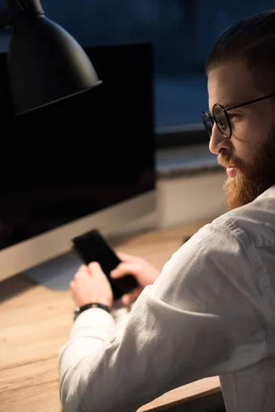 Gutaussehender Geschäftsmann nutzt Smartphone im Büro und schaut weg — Stockfoto