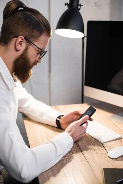 Hombre de negocios guapo usando teléfono inteligente en la oficina - foto de stock