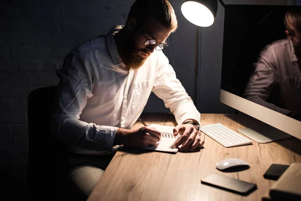 Geschäftsmann schreibt abends im Büro etwas ins Notizbuch — Stockfoto