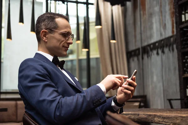 Bel homme en costume élégant en utilisant smartphone au restaurant — Photo de stock