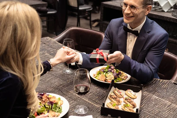 Happy adult man presenting valentines day gift to girlfriend at restaurant — Stock Photo