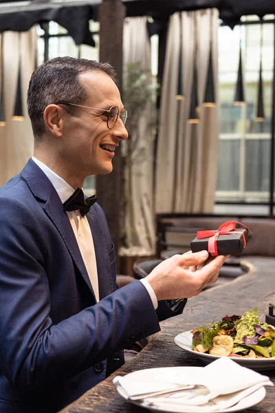 Красивый мужчина в стильном костюме представляет подарок на день Святого Валентина в ресторане — стоковое фото