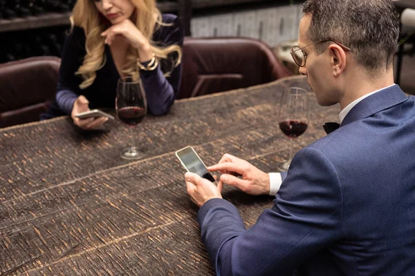 Casal adulto infeliz usando smartphones na data no restaurante — Fotografia de Stock