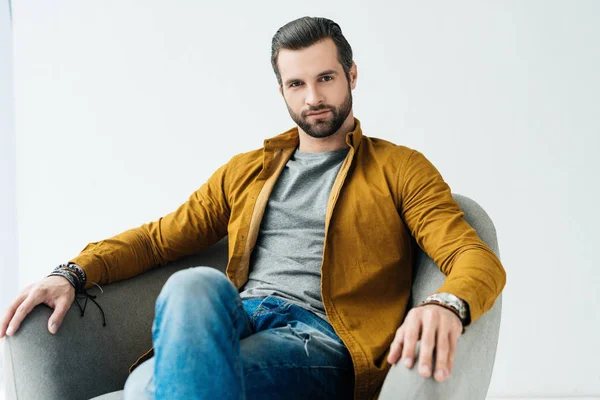 Handsome man sitting in armchair and looking at camera — Stock Photo