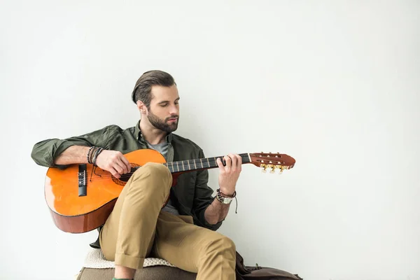 Bell'uomo che suona la chitarra acustica e appoggiato alla parete isolato sul bianco — Foto stock