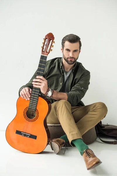 Handsome man holding acoustic guitar and looking at camera on white — Stock Photo