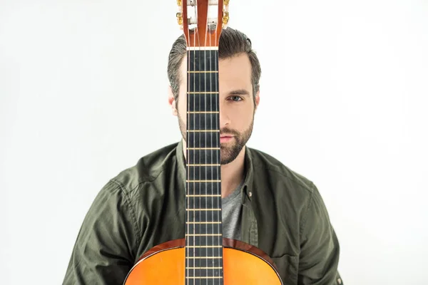 Handsome man covering eye with acoustic guitar neck and looking at camera isolated on white — Stock Photo