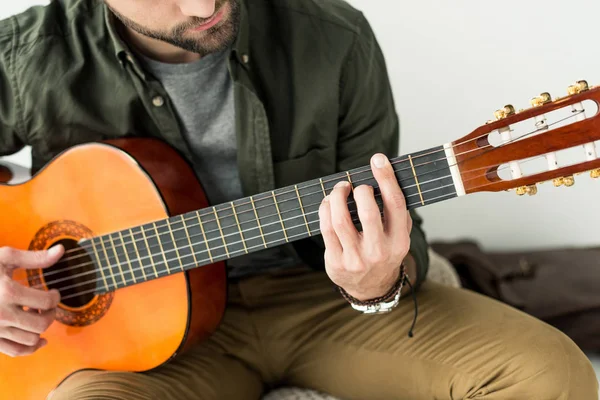 Imagen recortada del hombre tocando el acorde de la barra en la guitarra acústica - foto de stock