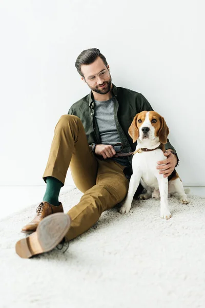 Schöner Mann umarmt niedlichen Beagle auf Teppich — Stockfoto