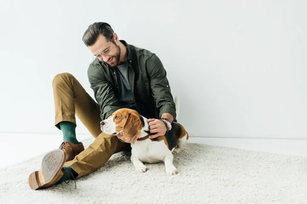 Lächelnder schöner Mann spielt mit süßem Beagle auf Teppich — Stockfoto