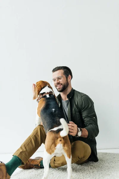 Красивый улыбающийся мужчина играет с собакой на ковре — стоковое фото