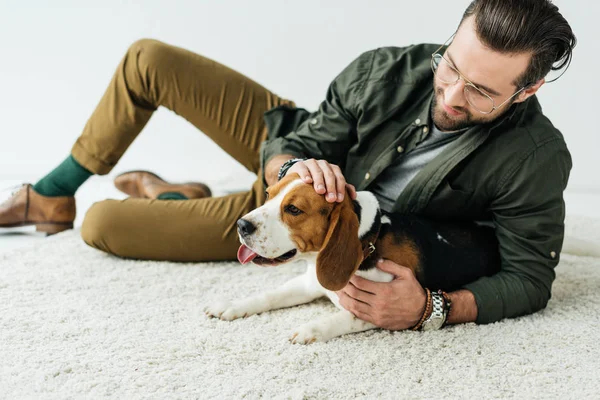 Bonito homem deitado no tapete e palmando bonito beagle — Fotografia de Stock