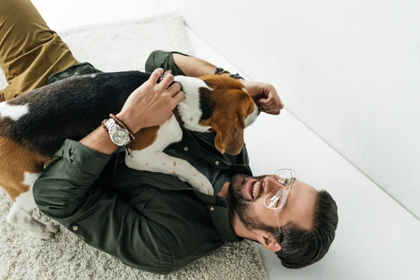 Blick aus der Vogelperspektive auf einen lächelnden Mann, der auf Teppich liegt und mit Hund spielt — Stockfoto