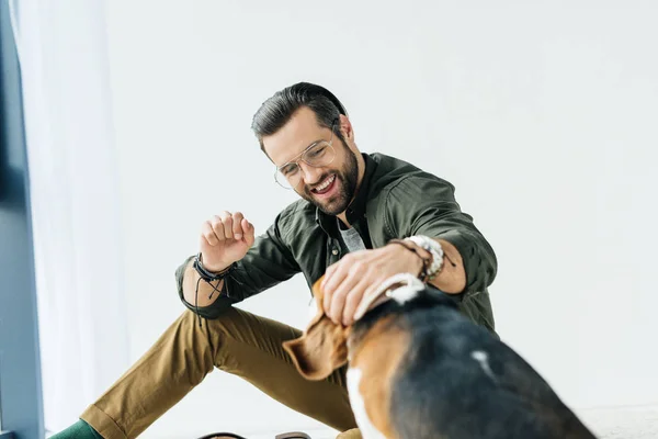 Счастливый человек, сидящий на полу и играющий с собакой — стоковое фото