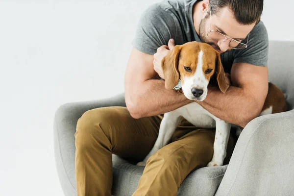 Чоловік обіймає собаку і сидить на кріслі ізольовано на білому — стокове фото