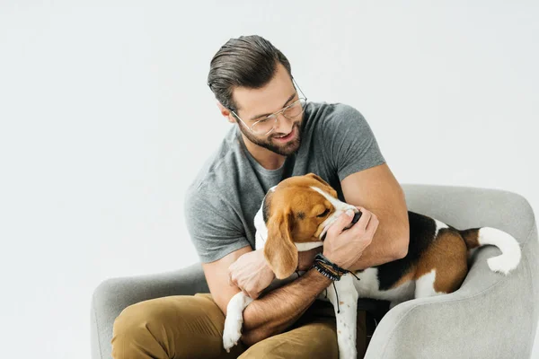 Sonriente guapo hombre jugando con perro en sillón aislado en blanco - foto de stock