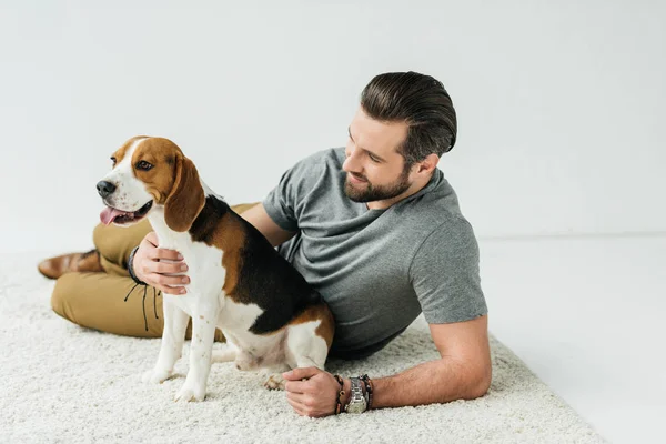 Schöner Mann umarmt niedlichen Beagle auf Teppich — Stockfoto