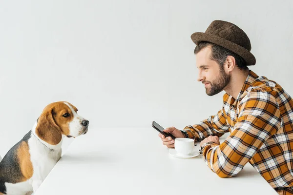 Side view of man holding smartphone at table with dog — Stock Photo