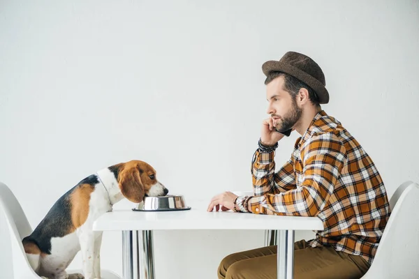 Side view of man talking by smartphone at table with dog — Stock Photo