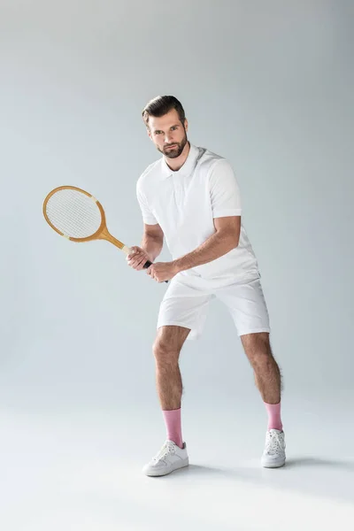 Guapo tenista con raqueta de tenis mirando a la cámara en gris - foto de stock