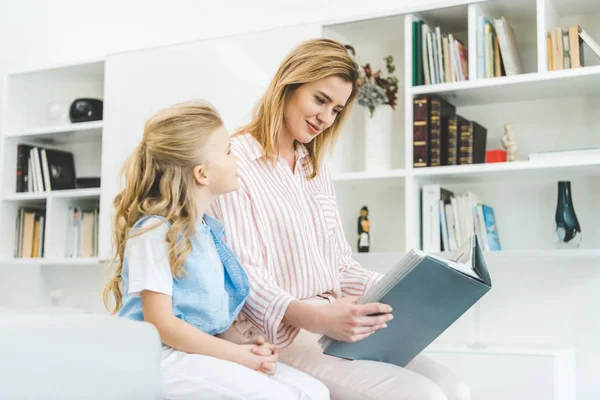 Mother reading book to daughter while resting on sofa at home — Stock Photo