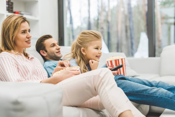 Боковой вид на семью с кукурузой, которая смотрит кино вместе дома — стоковое фото