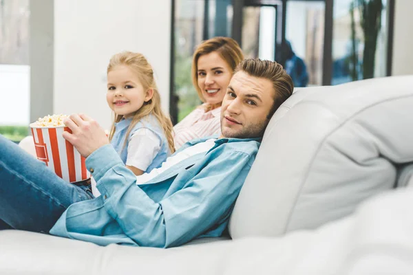 Seitenansicht einer Familie mit Popcorn, die in die Kamera schaut, während sie zu Hause gemeinsam Filme guckt — Stockfoto