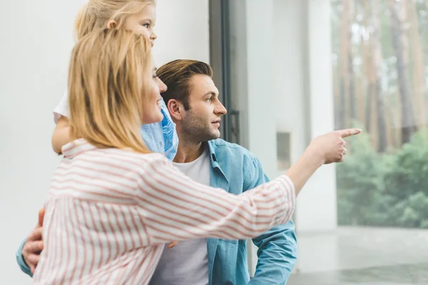 Side view of family looking out window together at home — Stock Photo