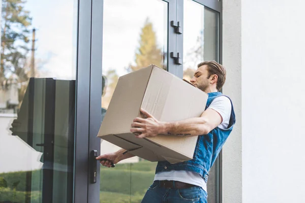 Hombre con caja de cartón que abre la puerta de la casa nueva - foto de stock
