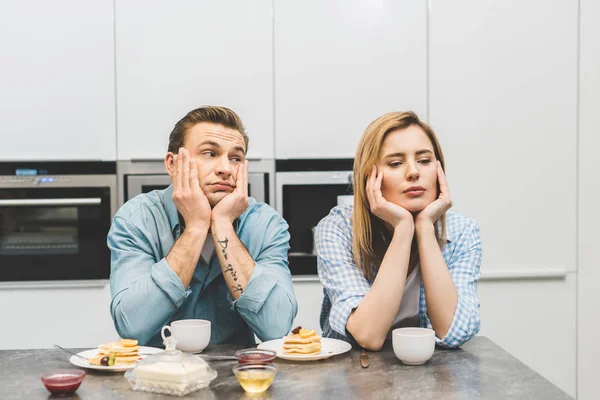 Retrato de pareja discutida sentada en la mesa con desayuno en casa - foto de stock