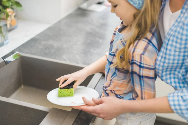 Schnappschuss von kleiner Tochter hilft Mutter nach dem Abendessen in Küche beim Geschirrspülen — Stockfoto