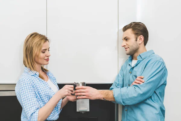 Vue latérale de la femme donnant tasse au mari dans la cuisine à la maison — Photo de stock