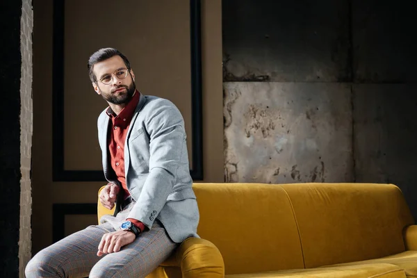 Handsome fashionable man in glasses and suit sitting on couch — Stock Photo