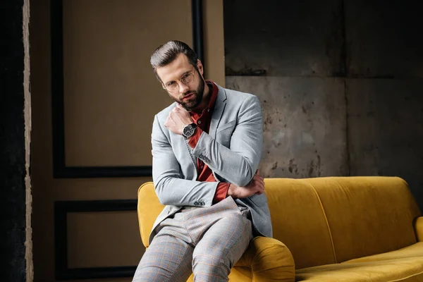 Homem elegante bonito em óculos e terno sentado no sofá — Stock Photo