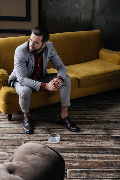 Homme élégant à la mode avec cigare et cendrier assis sur le canapé — Stock Photo