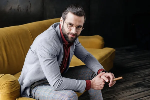 Fashionable bearded man with cigar sitting on couch — Stock Photo