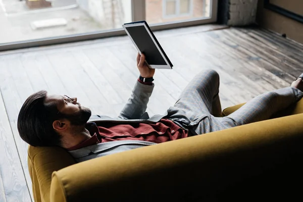 Schicker schöner Mann mit digitalem Tablet im Liegen auf der Couch — Stockfoto