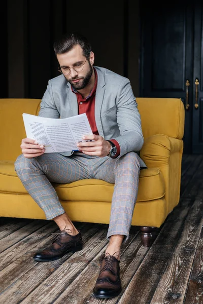 Handsome stylish man in trendy suit reading newspaper and sitting on couch — Stock Photo