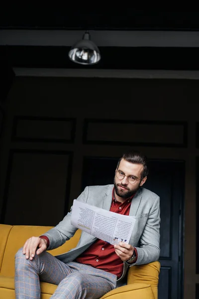 Homem na moda em terno moderno ler jornal e sentado no sofá — Fotografia de Stock