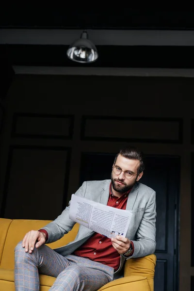 Fashionable man in trendy suit reading newspaper and sitting on couch — Stock Photo