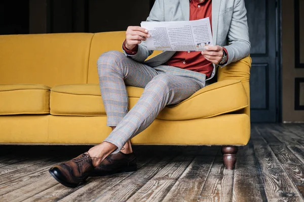 Ausgeschnittene Ansicht eines stilvollen Mannes, der auf einer Couch mit Zeitung sitzt — Stockfoto