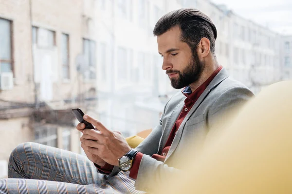 Schicker gutaussehender Mann sitzt mit Smartphone am Fenster — Stockfoto
