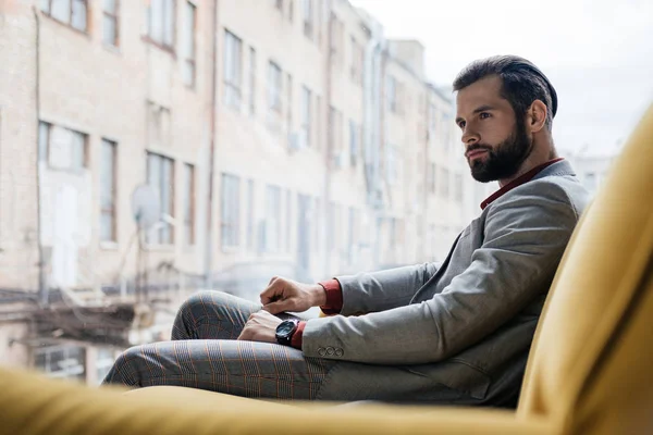 Stylish pensive man sitting on yellow sofa at window — Stock Photo