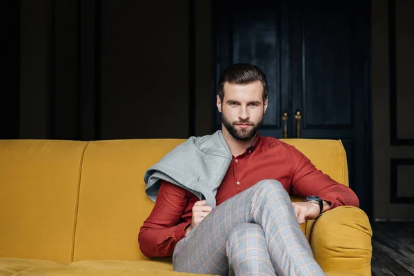 Fashionable man sitting on yellow sofa and looking at camera — Stock Photo