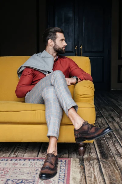 Homme à la mode en costume et chaussures de brogue assis sur un canapé jaune dans l'intérieur du loft — Stock Photo