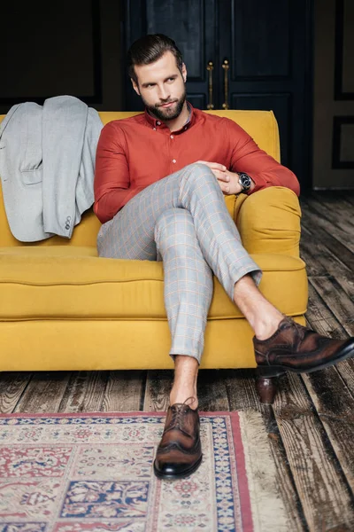 Hombre elegante en traje y zapatos brogue sentado en sofá amarillo - foto de stock